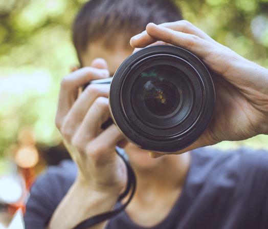 Mann mit Kamera vor dem Gesicht schaut direkt auf den Betrachter